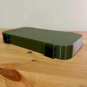Peut inclure: Un étui rectangulaire vert olive avec une surface texturée et des charnières noires. L'étui repose sur une surface en bois brun clair. L'étui semble être en plastique.