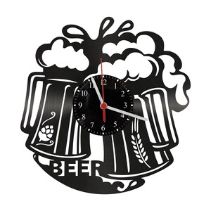 Może przedstawiać: Czarny zegar ścienny z motywem piwa. Zegar przedstawia dwa kufle piwa z pianą, tarczę zegara i napis "BEER". Wskazówki zegara są czerwone.