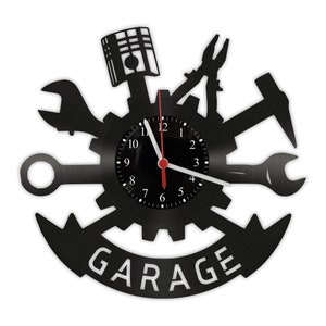 Könnte beinhalten: Schwarze Schallplattenuhr mit Zahnrad-Design und verschiedenen Werkzeugen, darunter ein Schraubenschlüssel, eine Zange und ein Hammer. Das Zifferblatt der Uhr ist weiß mit schwarzen Zahlen und Zeigern. Das Wort "GARAGE" ist in weißen Buchstaben auf einem schwarzen Banner geschrieben.