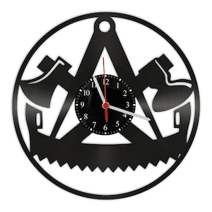 Puede incluir: Reloj de vinilo negro con un diseño de hacha, sierra y compás. La esfera del reloj es negra con números y manecillas blancas.