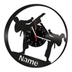 Könnte beinhalten: Schwarze Schallplattenuhr mit zwei Silhouetten von Personen in einer Kampfkunstpose. Das Zifferblatt der Uhr ist schwarz mit weißen Zahlen und Zeigern. Der Text "Name" ist unten auf der Uhr gedruckt.