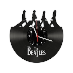 Puede incluir: Reloj de vinilo negro con una silueta de los Beatles caminando por un paso de cebra, con el nombre de la banda "The Beatles" impreso debajo de la esfera del reloj.