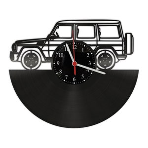 Può includere: Un orologio in vinile nero con una silhouette bianca di una jeep sulla metà superiore. Il quadrante dell'orologio è nero con numeri e lancette bianchi.