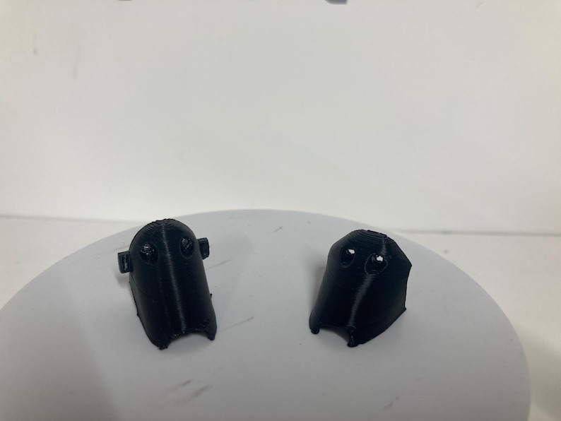 Puede incluir: Dos componentes de pl&aacute;stico negro impresos en 3D con una forma curva y c&oacute;nica, que presentan dos peque&ntilde;as hendiduras circulares cerca de la parte superior. Cada pieza tiene un acabado mate liso y una cresta vertical en el centro.