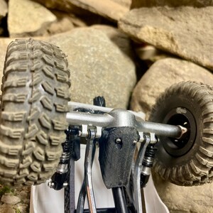 Puede incluir: Un chasis de veh&iacute;culo de radiocontrol para rocas con un eje de metal plateado, neum&aacute;ticos todoterreno negros texturizados y una cubierta de diferencial negra impresa en 3D. El sistema de suspensi&oacute;n incluye amortiguadores negros.