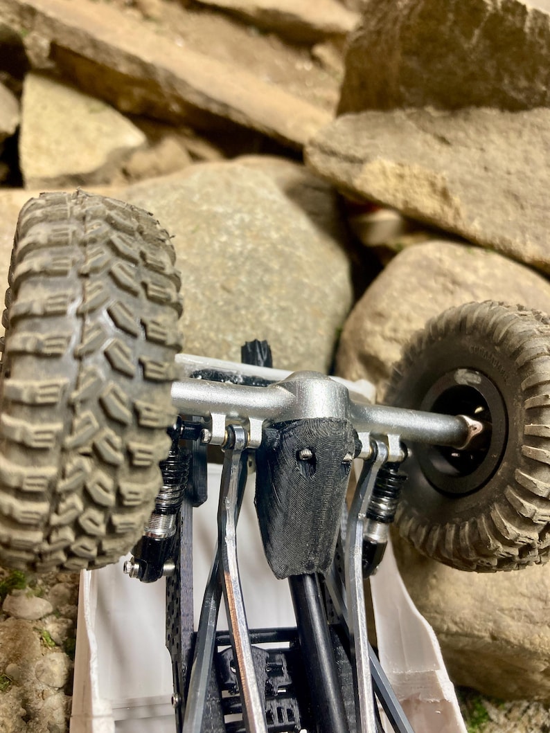 Puede incluir: Un chasis de veh&iacute;culo de radiocontrol para rocas con un eje de metal plateado, neum&aacute;ticos todoterreno negros texturizados y una cubierta de diferencial negra impresa en 3D. El sistema de suspensi&oacute;n incluye amortiguadores negros.