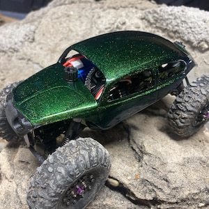 以下が含まれることがあります： 緑色のグリッターでコーティングされたカスタムペイントのオフロードリモートコントロールカー。黒いタイヤと紫色のアクセントが特徴です。