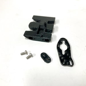 Puede incluir: Un conjunto de piezas de plástico negro y fibra de carbono para un dron u otra aeronave pequeña. El conjunto incluye un marco de plástico negro, dos tornillos negros, un espaciador de plástico negro y un brazo de fibra de carbono.