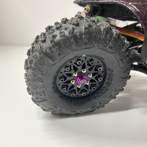 May include: Close-up of a black tire with a black and silver rim. The tire has a tread pattern and the rim has a purple center cap.