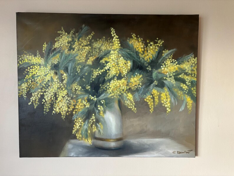 May include: A painting of a bouquet of yellow mimosa flowers in a white vase with a gold trim. The flowers are arranged in a loose, natural style and the background is a soft brown.