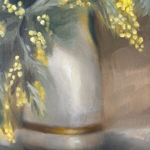 May include: A white ceramic vase with a gold band around the rim, filled with yellow mimosa flowers.