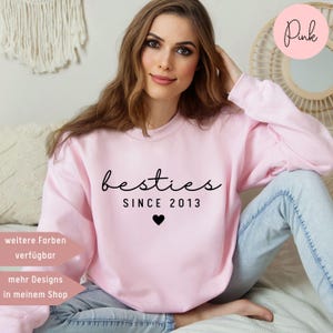 Könnte beinhalten: Rosafarbener Pullover mit dem Text "besties since 2013" und einem kleinen schwarzen Herz. Der Pullover wird von einer Person getragen.