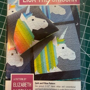 May include: A package for a quilt and pillow pattern featuring a unicorn design. The package has the text "LISA THE UNICORN" and "A PATTERN BY ELIZABETH HARTMAN". The unicorn has a rainbow mane and a white body. The pattern uses precut fabric strips.