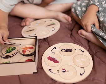 May include: A wooden box with a set of wooden puzzle pieces featuring different stages of insect life cycles. The pieces are arranged in a circle with arrows showing the direction of the life cycle. The box is open and the pieces are visible. Two children are playing with the puzzle on a brown blanket.