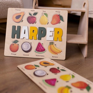 May include: A wooden puzzle with a name, "HARPER", spelled out in colorful letters. The puzzle features different fruits, including a papaya, apple, pear, mango, orange, coconut, watermelon, and banana. Each fruit has its name written below it.