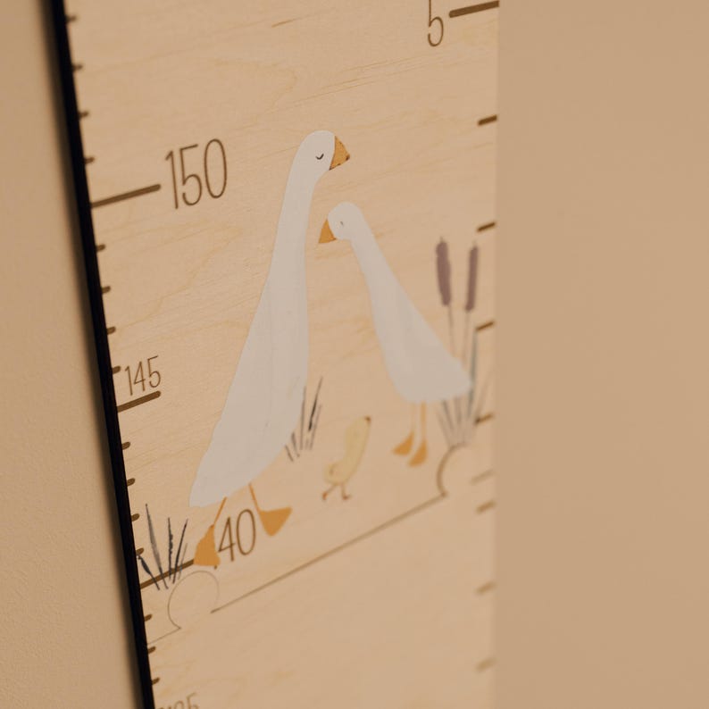May include: Wooden height chart with a painted illustration of two white geese with orange beaks and feet. The chart has black measurement markings and numbers, with the highest measurement at 150 inches. The background is a light beige color.