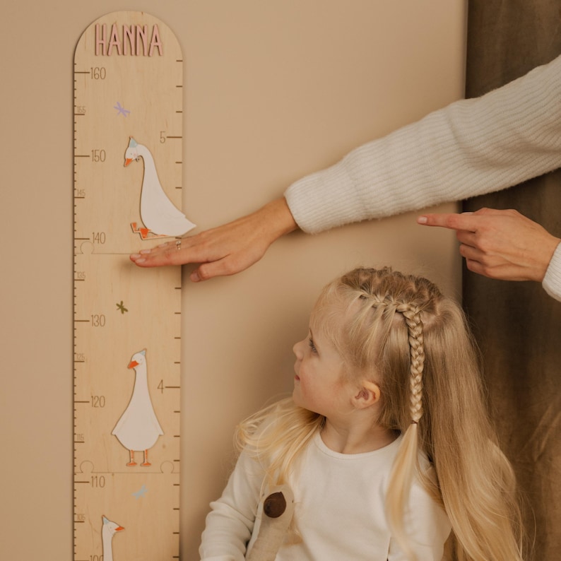 May include: Wooden growth chart with the name "Hanna" at the top. The chart features goose illustrations and dragonfly accents. The height is measured in centimeters, with a maximum height of 160 cm.