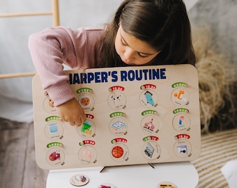 May include: A wooden activity board with the text "Harper's Routine" printed on it. The board has a series of circles with different images and the words "Done" and "To Do" printed on them. A young girl is interacting with the board, moving a small wooden token with an image of a green trash can.