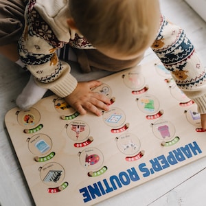 May include: A wooden activity board with a blue and white banner that reads "HARPER'S ROUTINE". The board has a series of circular slots with images and text that say "TO DO" and "DONE". A child is interacting with the board by moving the sliders.