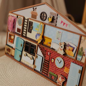 May include: Wooden dollhouse with multiple rooms, featuring a red brick wall, blue doors, and various decorative elements. Includes a clock, a dog, and a bed. The name "PEARL" is written on the roof.
