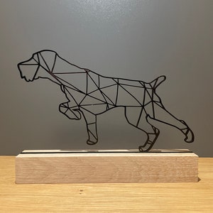 Könnte beinhalten: Eine schwarze Metallskulptur eines Hundes im geometrischen Stil, die auf einem Holzsockel steht.