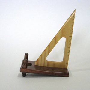 May include: A wooden triangle ruler with a dark brown base and three wooden pegs. The ruler is made of light wood with a striped pattern.