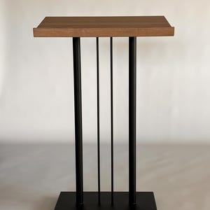 Puede incluir: Un atril de madera con una base de metal negro y cuatro patas. La base tiene tres barras de metal verticales.