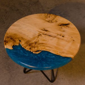 May include: Round wooden table with a blue epoxy resin inlay. The table has a black metal tripod base.