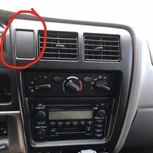 Könnte beinhalten: Nahaufnahme eines Auto-Armaturenbretts mit Lüftungsschlitzen, einem Radio und verschiedenen Bedienknöpfen. Das Armaturenbrett ist hauptsächlich schwarz und grau, mit einem rechteckigen Staufach. Das Radio hat einen CD-Player und AM/FM-Radio.