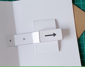 May include: A white paper pop-up card template featuring a sliding mechanism. The mechanism includes a rectangular tab with the letters A and H printed on a hatched background, connected to a white strip with a black arrow pointing to the right.