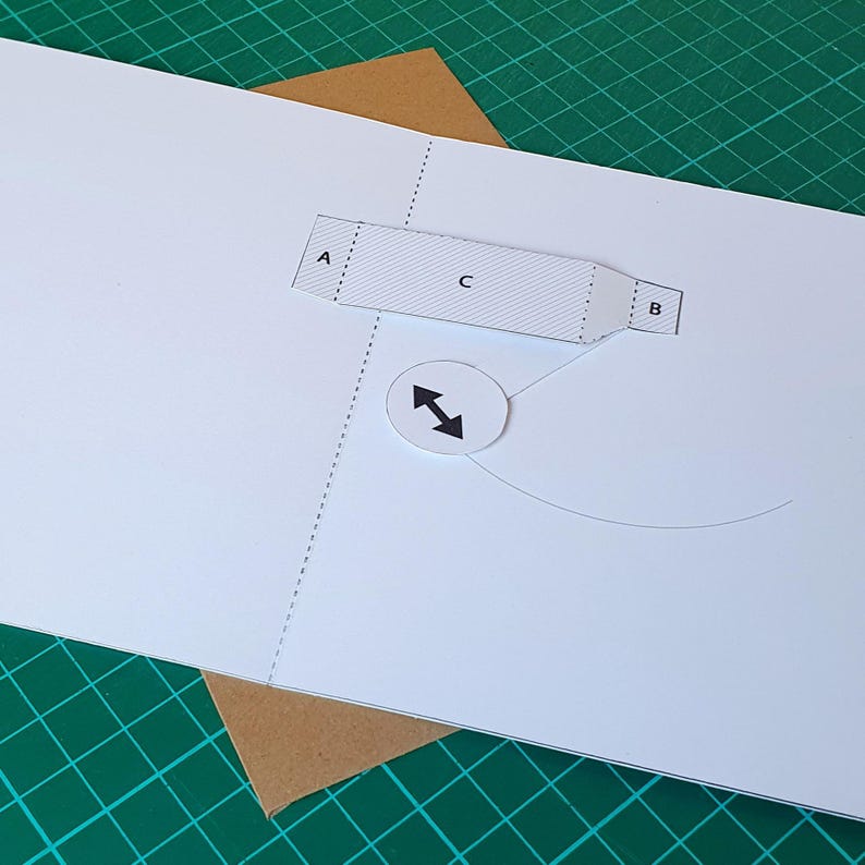 May include: A white paper template featuring a rectangular section labelled A, C, and B with diagonal line patterns. A circular white cutout with a black double-headed arrow icon is positioned below the rectangle, connected by a thin curved line.