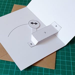 May include: A white paper pop-up card template featuring a three-dimensional bridge structure labelled with the letters A, B, and C. The design includes a circular icon with a double-headed arrow and a curved line, with dashed fold lines.