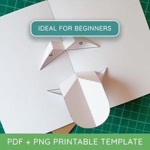 Op de afbeelding: Een wit papieren pop-up knutseltemplate met gevouwen secties gemarkeerd met de letters C en D. Een blauwgroene rechthoekige banner bovenaan bevat de witte tekst IDEAL FOR BEGINNERS. Onderaan staat de tekst PDF + PNG PRINTABLE TEMPLATE.