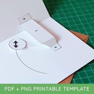 Op de afbeelding: Een pop-up kaart sjabloon van wit papier met een rechthoekig gedeelte gelabeld met de letters A, B en C, en een cirkelvormig lipje met een zwart dubbelzijdig pijlicoon. Het ontwerp bevat gestippelde vouwlijnen en een gebogen zwarte hulplijn.