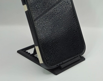 Op de afbeelding: Een zwarte telefoonhoes met een witte streep staat op een zwarte telefoonstandaard. De telefoonhoes heeft een getextureerd oppervlak.