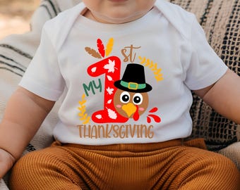 May include: A white baby onesie with a red and brown turkey graphic. The onesie says "My 1st Thanksgiving".
