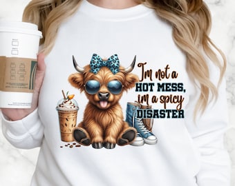 Pode incluir: Camisola branca com uma vaca das terras altas de desenho animado usando óculos de sol e um laço azul. A vaca está segurando uma bebida de café. O texto "I'm not a hot mess, I'm a spicy disaster" está impresso na camisola.