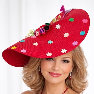 May include: A wide-brimmed red straw hat featuring a cluster of fabric flowers in shades of pink, purple, and green on the side, accented with scattered small felt flower cutouts in various colours including white, blue, yellow, and pink.