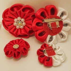 May include: Four handmade fabric flower brooches. Two are red, one with pearl and rhinestone accents. The other two are red and white, with pin backs. These decorative accessories can be used to embellish clothing or accessories.