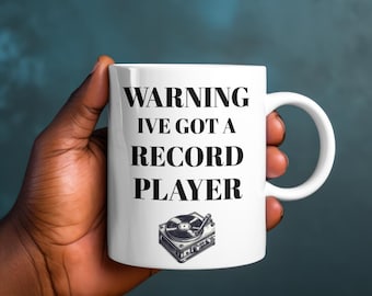 May include: White ceramic mug with black text that reads "WARNING I'VE GOT A RECORD PLAYER" and a black and white illustration of a record player.