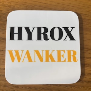 May include: White square coaster with the words "HYROX WANKER" printed in black and orange letters.
