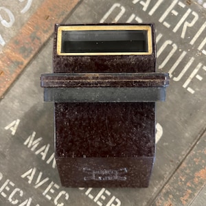 Puede incluir: Un visor estereoscópico vintage de plástico marrón con un borde dorado alrededor de la ventana de visualización. El visor tiene una base de goma negra y un logotipo con espadas cruzadas y el texto "Stereoscope" en la parte delantera.