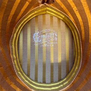 May include: Close-up of a vintage hat's interior, showcasing a striped pattern in gold and brown. The hat's lining includes a label with the name "Condolff" and the address "Rue Serpenoise 15, METZ".