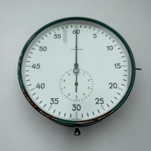 May include: A vintage Junghans stopwatch with a white face, black hands, and green trim. The watch features a large main dial with numbers from 0 to 60 and a smaller subdial. The words "MADE IN GERMANY" are visible.