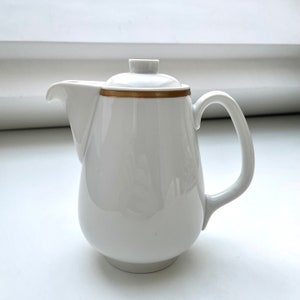 May include: White ceramic creamer with a gold trim around the top. The creamer has a rounded body and a handle.