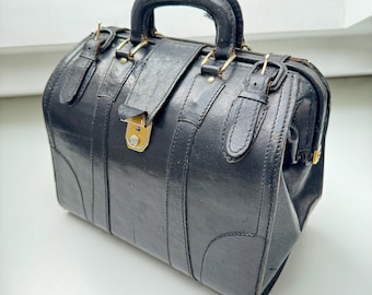 May include: A black leather doctor's bag with brass hardware and a buckle closure.