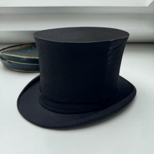 May include: A black top hat, a traditional formal headwear item. It features a cylindrical crown and a gently curved brim. The hat has a black band around the base of the crown. The hat is a classic formal accessory.