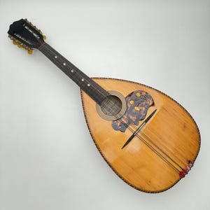 Può includere: Un mandolino vintage in legno con un intarsio madreperlaceo attorno al foro sonoro. Il mandolino ha una finitura in legno naturale e una tastiera di colore marrone scuro.