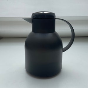 Könnte beinhalten: Eine schwarze Thermokanne mit schwarzem Deckel und Griff. Die Kanne ist aus Edelstahl und hat ein elegantes, modernes Design.
