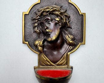 Könnte beinhalten: Eine Messingwandplakette mit einer Reliefskulptur von Jesus Christus, der eine Dornenkrone trägt. Die Plakette hat einen kleinen, rot ausgekleideten Messingbecher, der unten angebracht ist.